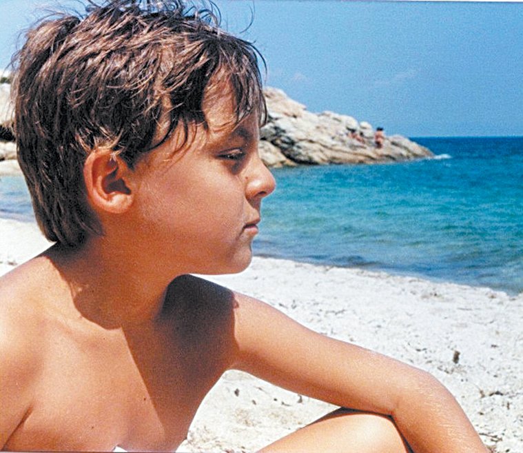 Απεικονίζεται ο Αύγουστος Κουρτώ παιδί, καθισμένος σε μία παραλία της Χαλκιδικής