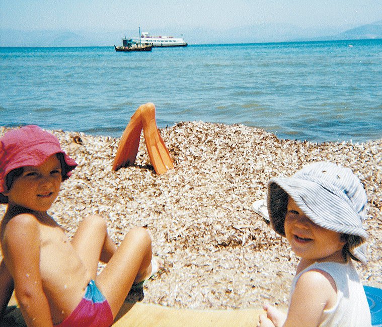 Απεικονίζεται ο Στάθης Δρογώσης παιδί να κάθεται στην παραλία της Ίο