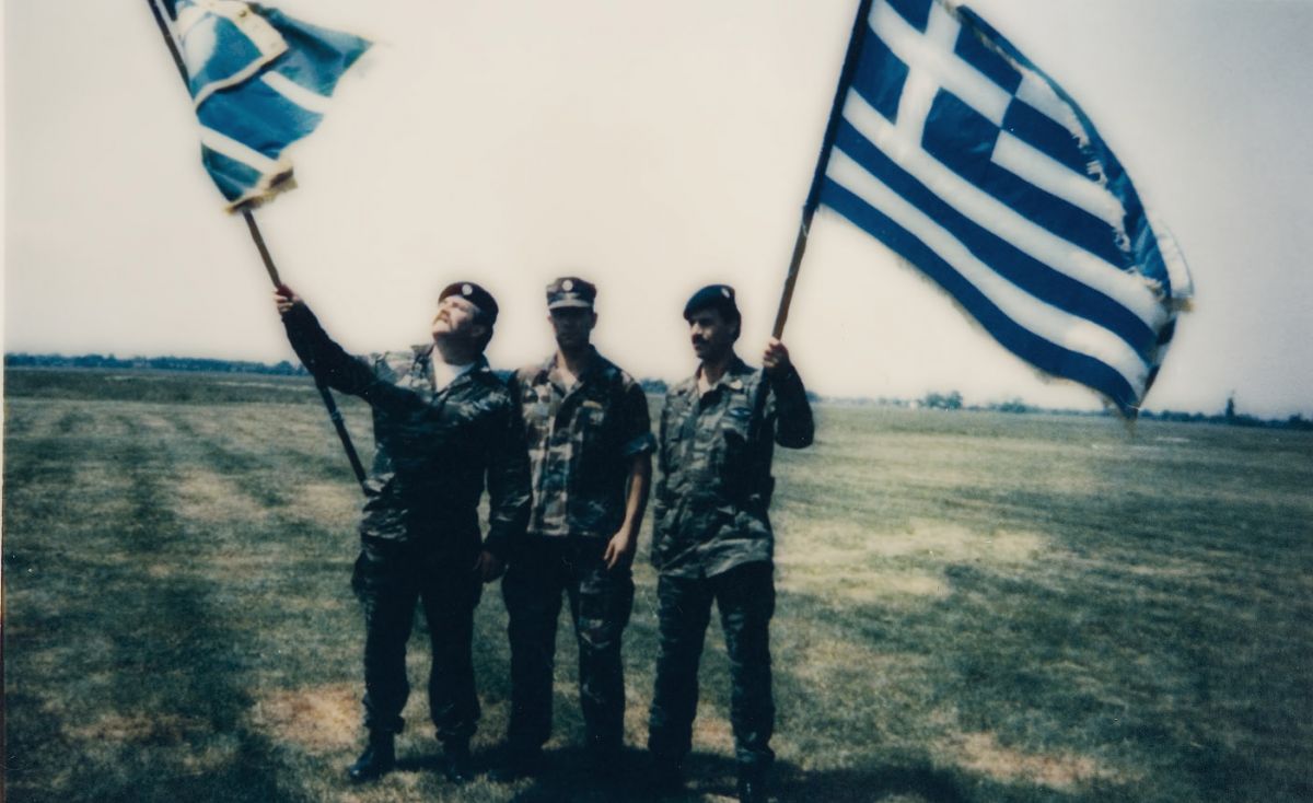 Απεικονίζονται τρεις στρατιώτες που κρατούν ελληνικές σημαίες